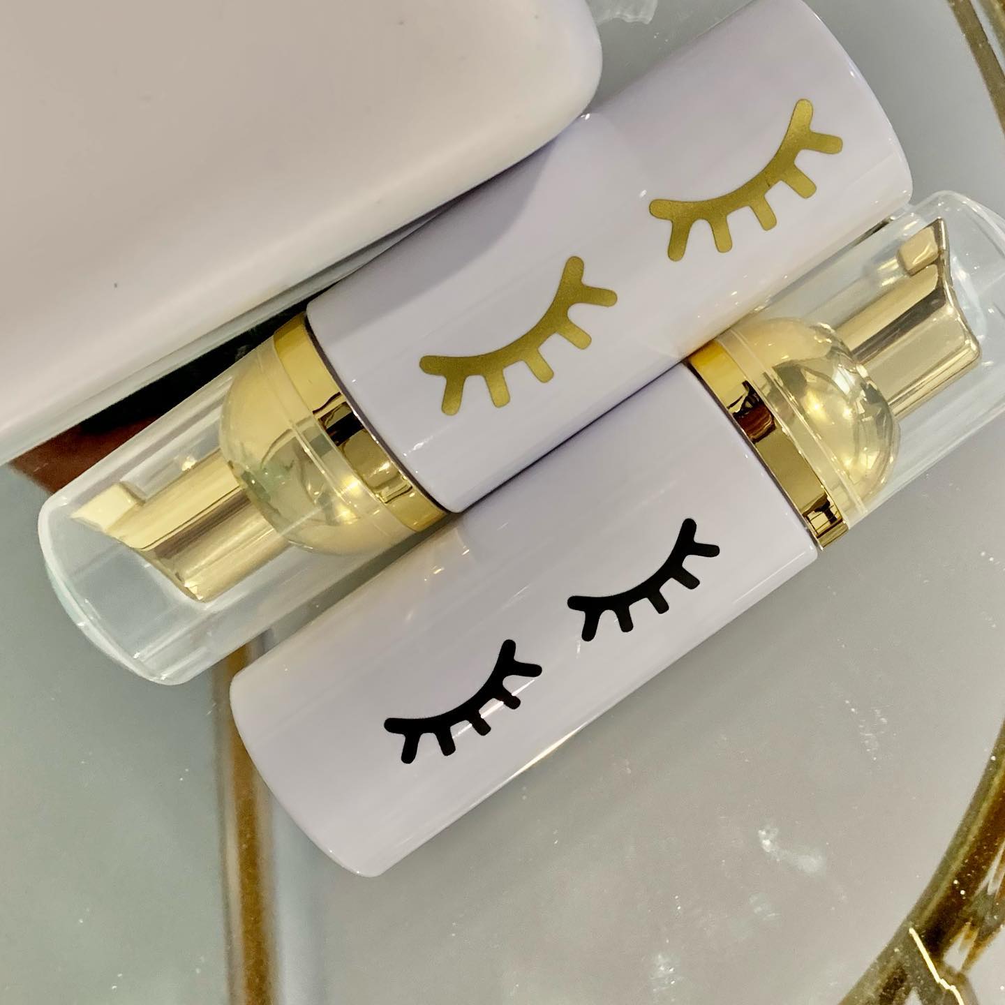 Gold and white lash foam cleanser bottles